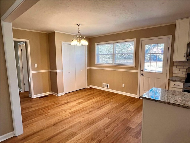 unfurnished dining area with a textured ceiling, light hardwood / wood-style flooring, a notable chandelier, and crown molding