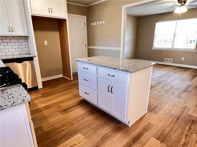 kitchen with backsplash, white cabinets, stainless steel dishwasher, a kitchen island, and light stone counters