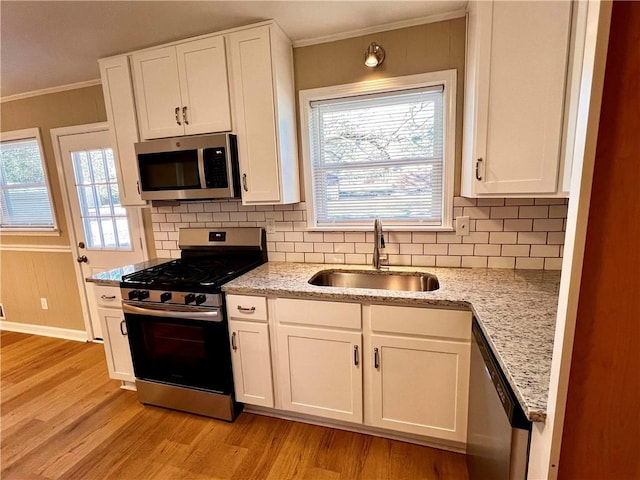 kitchen with appliances with stainless steel finishes, light stone counters, sink, light hardwood / wood-style flooring, and white cabinets