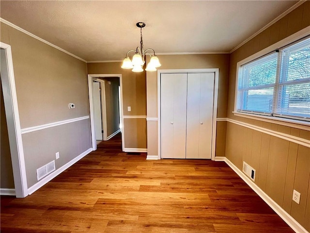 unfurnished bedroom with crown molding, a closet, hardwood / wood-style floors, and a notable chandelier