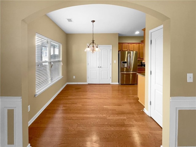 unfurnished dining area with arched walkways, visible vents, baseboards, light wood-style floors, and an inviting chandelier