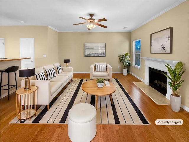 living area featuring baseboards, ceiling fan, ornamental molding, light wood-style floors, and a fireplace