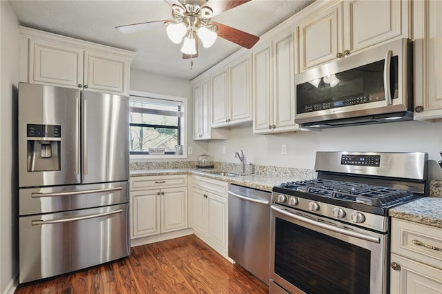 kitchen with light stone countertops, dark wood-style floors, stainless steel appliances, a ceiling fan, and a sink