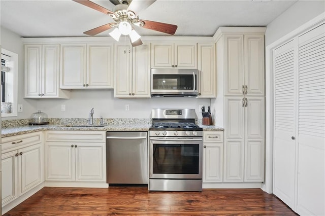 kitchen with dark wood-style floors, stainless steel appliances, light stone counters, and a sink