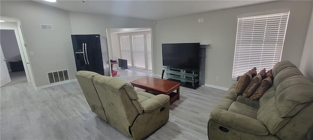 living room with visible vents, baseboards, light wood-style flooring, and vaulted ceiling