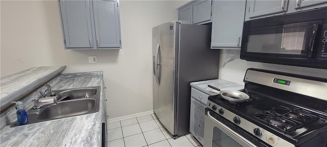 kitchen featuring baseboards, light countertops, light tile patterned floors, stainless steel appliances, and a sink