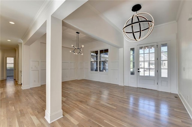 foyer entrance featuring crown molding, wainscoting, a decorative wall, light wood-style floors, and a notable chandelier