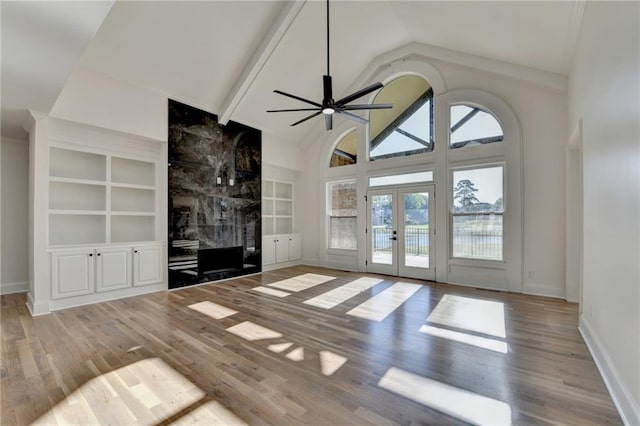 unfurnished living room with plenty of natural light, wood finished floors, built in shelves, and french doors