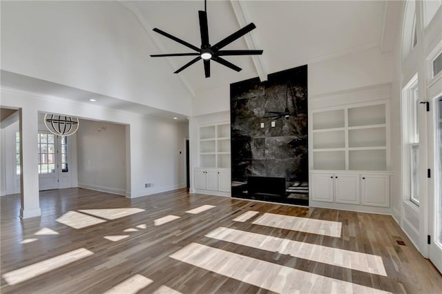 unfurnished living room with wood finished floors, baseboards, high vaulted ceiling, built in shelves, and ceiling fan with notable chandelier