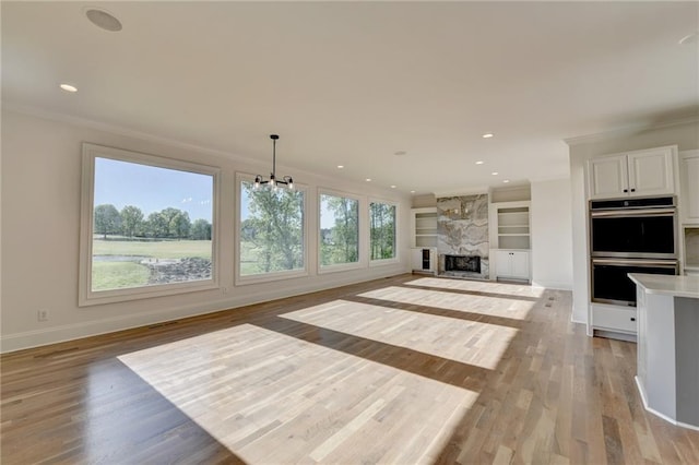 unfurnished living room with crown molding, baseboards, built in shelves, and light wood-type flooring