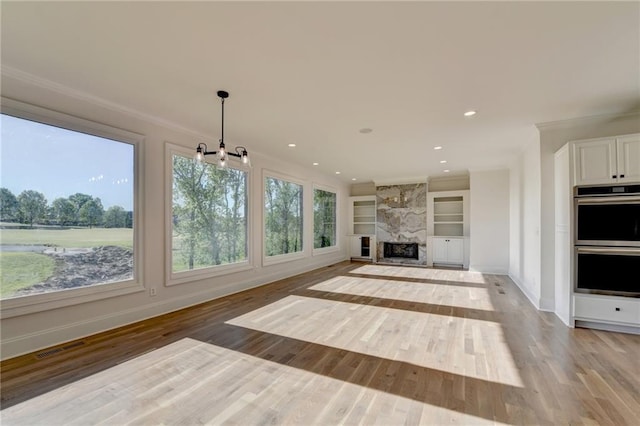 unfurnished living room with baseboards, ornamental molding, built in features, and light wood-type flooring