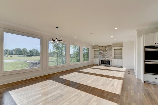 unfurnished living room with light wood-type flooring, ornamental molding, built in features, and baseboards