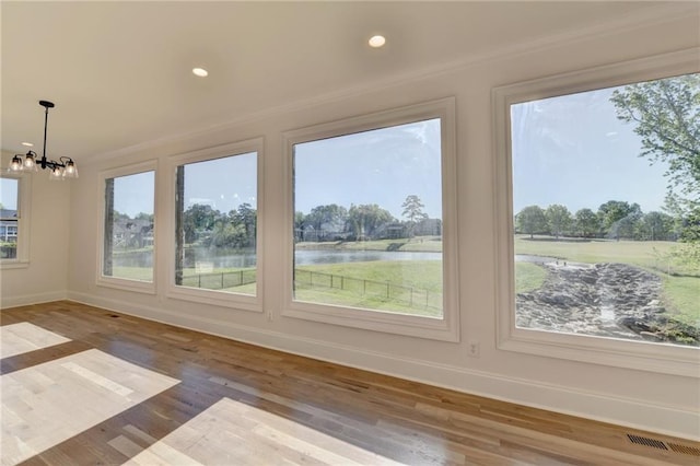 unfurnished sunroom with crown molding, a notable chandelier, baseboards, wood finished floors, and a water view
