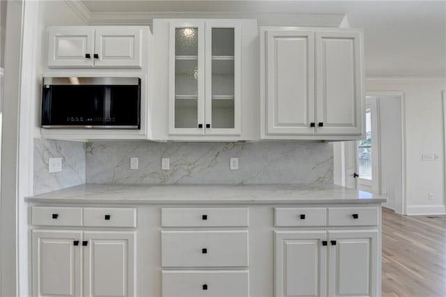 kitchen featuring light stone counters, white cabinets, ornamental molding, and backsplash
