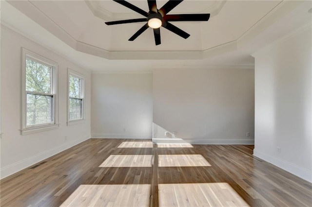 empty room featuring a ceiling fan, visible vents, wood finished floors, baseboards, and a tray ceiling