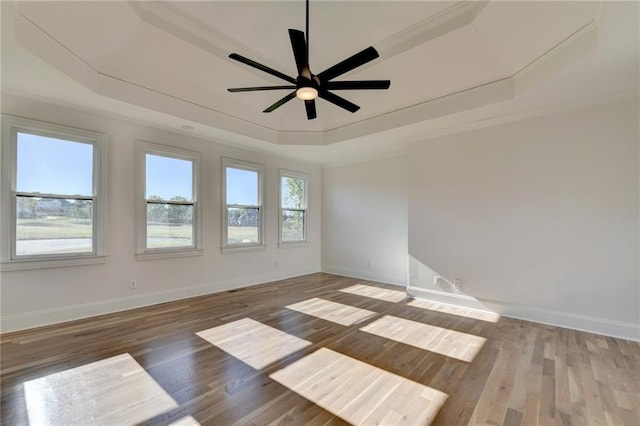 spare room featuring ornamental molding, wood finished floors, baseboards, ceiling fan, and a raised ceiling