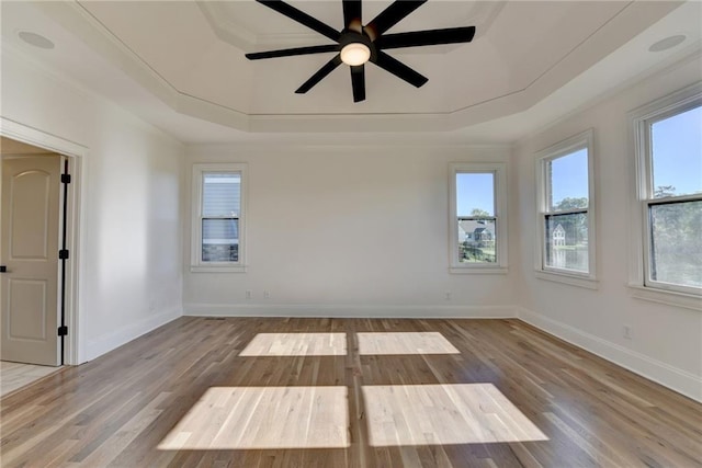 spare room featuring a raised ceiling, a ceiling fan, baseboards, wood finished floors, and ornamental molding