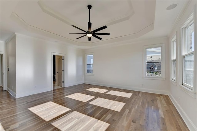 unfurnished room featuring ceiling fan, wood finished floors, a raised ceiling, baseboards, and ornamental molding