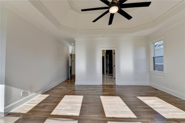 empty room featuring crown molding, wood finished floors, baseboards, ceiling fan, and a raised ceiling