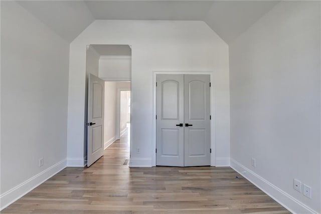 unfurnished bedroom featuring baseboards, light wood finished floors, and lofted ceiling