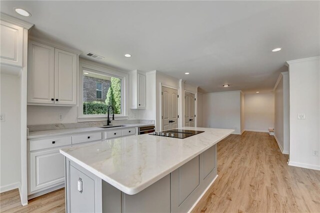 kitchen featuring black electric stovetop, a sink, light wood-style flooring, a center island, and visible vents