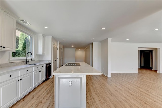 kitchen with visible vents, a center island, a sink, white cabinets, and light wood finished floors