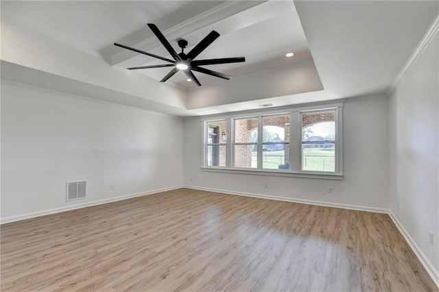 unfurnished room featuring a raised ceiling, baseboards, wood finished floors, visible vents, and ornamental molding