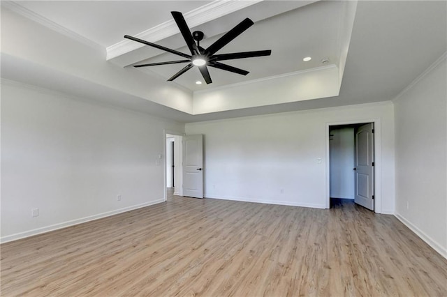 spare room with a tray ceiling, ornamental molding, baseboards, and light wood-style floors