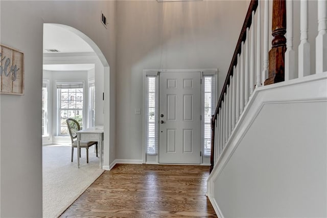 foyer entrance with stairway, arched walkways, visible vents, and wood finished floors