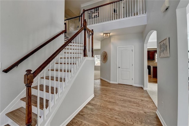 stairs with a high ceiling, wood finished floors, arched walkways, and baseboards