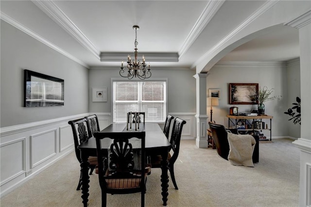 dining room with a chandelier, a tray ceiling, light carpet, arched walkways, and ornate columns