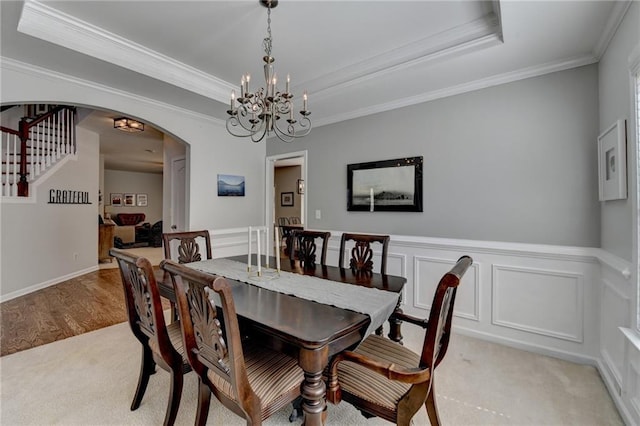 dining area with ornamental molding, a tray ceiling, arched walkways, an inviting chandelier, and stairs