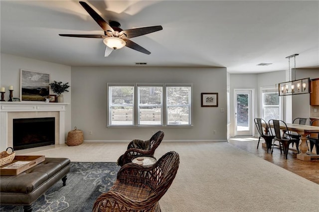 living room featuring visible vents, ceiling fan with notable chandelier, a fireplace with flush hearth, and carpet