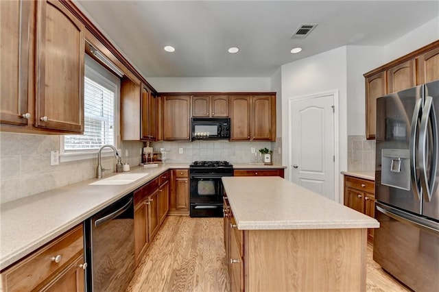 kitchen featuring visible vents, black appliances, light wood-style flooring, a sink, and a center island