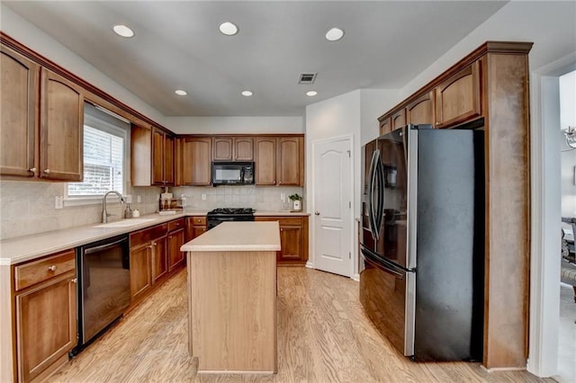 kitchen with visible vents, a kitchen island, a sink, black appliances, and light wood-style floors