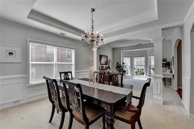 dining room with decorative columns, a raised ceiling, arched walkways, and light colored carpet