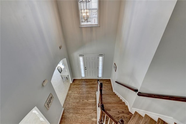 entrance foyer with wood finished floors, baseboards, stairs, a towering ceiling, and a notable chandelier