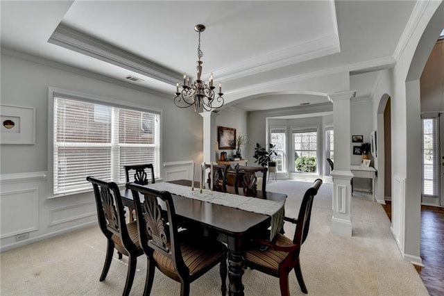 dining space with decorative columns, light carpet, arched walkways, a decorative wall, and a raised ceiling