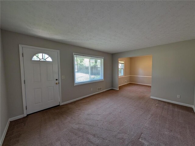 foyer entrance with visible vents, carpet, baseboards, and a textured ceiling