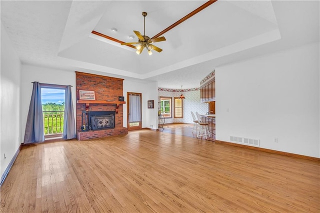 unfurnished living room with light wood-type flooring, plenty of natural light, a raised ceiling, a brick fireplace, and visible vents