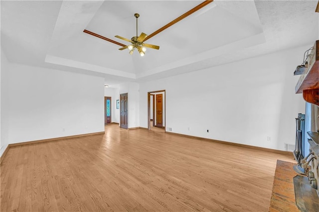 unfurnished living room with light wood finished floors, baseboards, a ceiling fan, and a tray ceiling