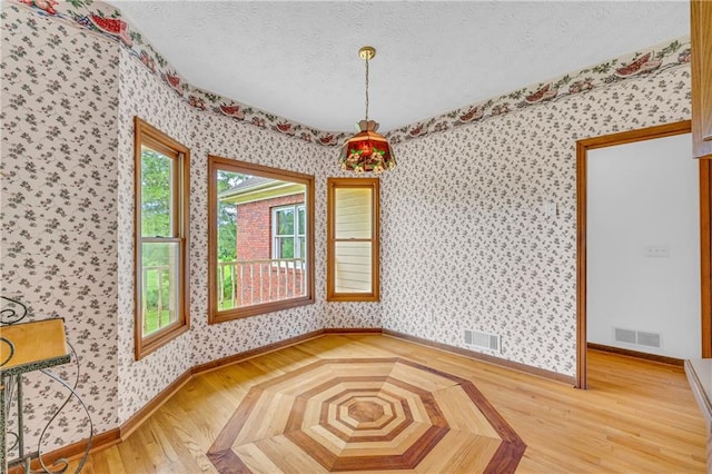 unfurnished dining area with a textured ceiling, parquet flooring, wallpapered walls, and visible vents