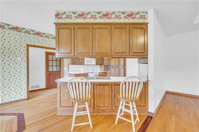 kitchen with a peninsula, light countertops, white appliances, wallpapered walls, and a kitchen breakfast bar