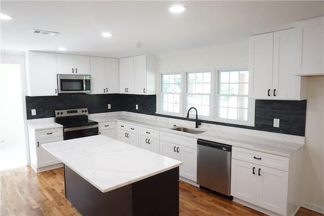 kitchen featuring light stone counters, stainless steel appliances, sink, a center island, and white cabinetry