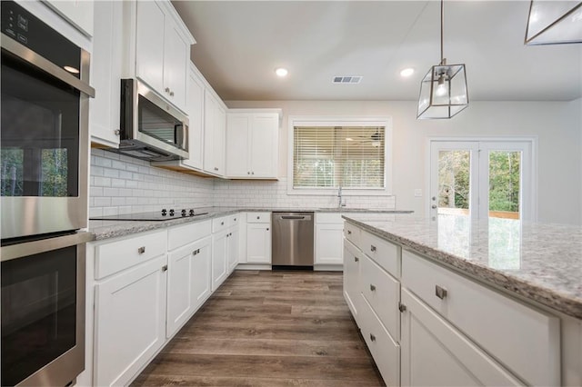 kitchen with light stone countertops, appliances with stainless steel finishes, white cabinets, and dark hardwood / wood-style flooring