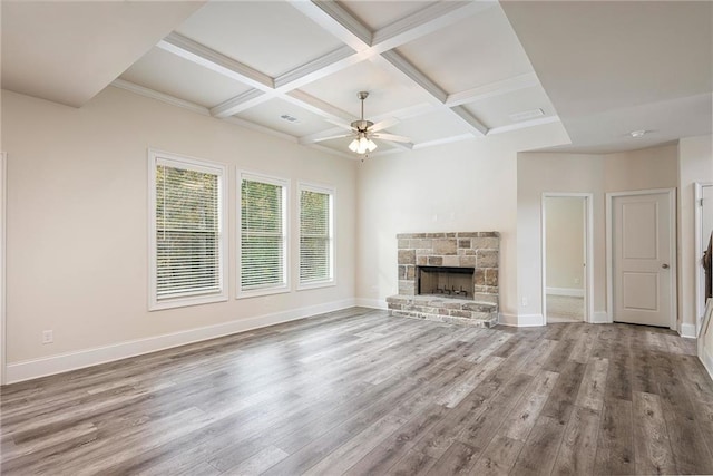 unfurnished living room with coffered ceiling, a stone fireplace, hardwood / wood-style flooring, and ceiling fan