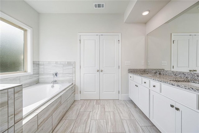 bathroom with vanity and tiled bath