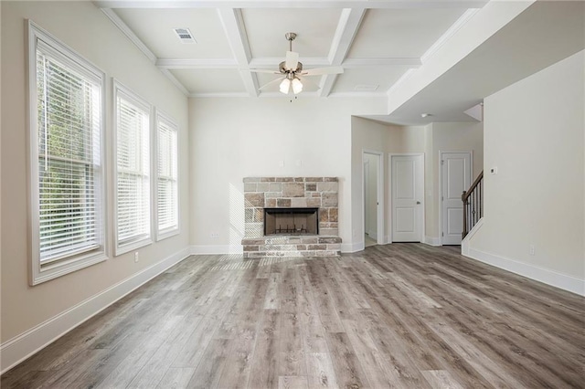 unfurnished living room featuring ceiling fan, hardwood / wood-style flooring, beamed ceiling, a stone fireplace, and coffered ceiling