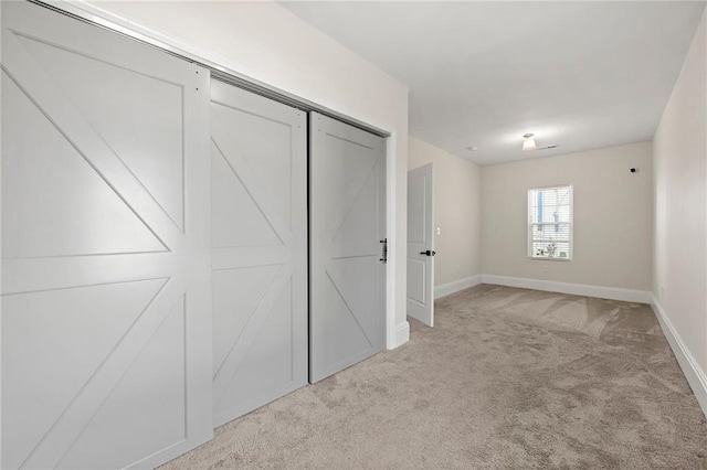 unfurnished bedroom with light carpet, a closet, and baseboards