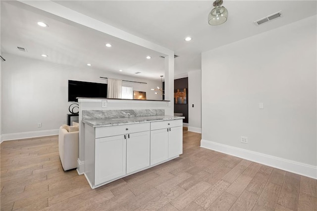 kitchen featuring light wood finished floors, visible vents, white cabinetry, and light stone counters